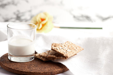 Milk in a transparent glass and healthy cookies with cereals on a cork wood stand. On a marble background.