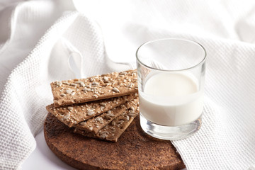 Milk in a transparent glass and healthy cookies with cereals on a cork wood stand. On a marble background.
