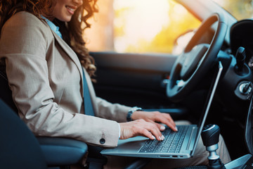 Beautiful young businesswoman driving car and using laptop.