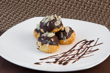 Choux pastry in chocolate glaze and thinly sliced almonds on a large white plate on a brown background