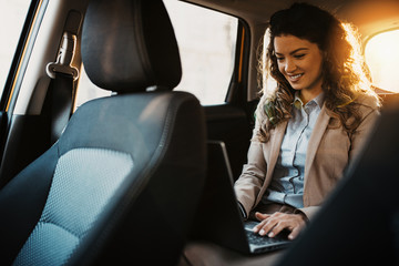 Fototapeta na wymiar Businesswoman using laptop in back seat of luxury car.