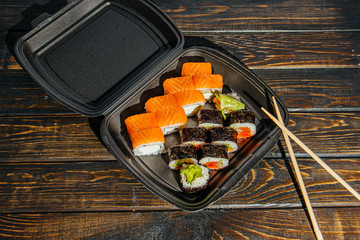 The concept of non-contact delivery of sushi rolls. Black packaging with different rolls and craft package on a wooden table.