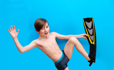 Boy in swimming flippers close-up on a blue background. Cheerful child on vacation at sea, in a water park, a tourist trip. Summer travel and vacation with children