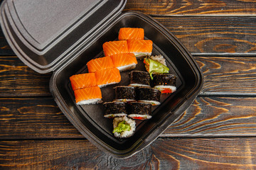 The concept of non-contact delivery of sushi rolls. Black packaging with different rolls and craft package on a wooden table.