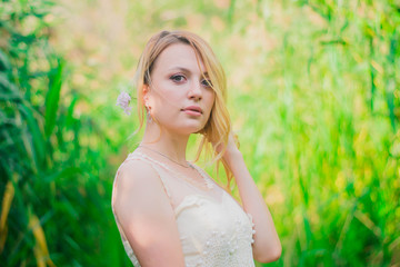 young, blonde girl, of Slavic origin, in a white dress of the bride against the background of summer green nature. A girl in a white dress among green trees in the forest