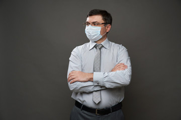 a man dressed as a businessman posing in a studio on a gray background, medical face mask, glasses, a light striped shirt and tie - casual office wear, concept of quarantine and antivirus protection