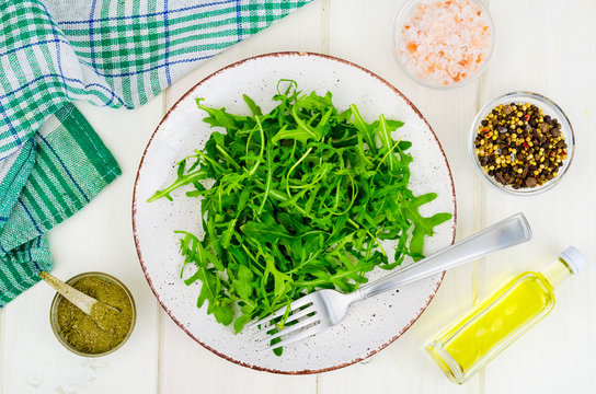 Vegetarian food. Fresh green arugula on plate, white wooden background.