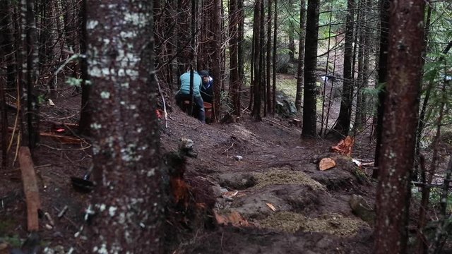 Two men pushing whellbarrow with dirt in forest, building a new trail.