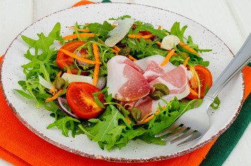 Plate with fresh salad leaves, parmesan slices and jamon. Studio Photo
