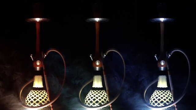 Three beautiful hookahs appear on a black background in multicolored smoke, slow motion