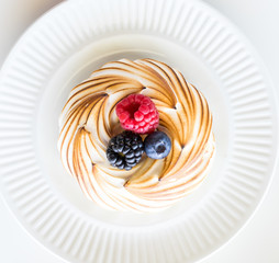 A top down macro view of a single meringue with berries on a white plate, ready for eating.