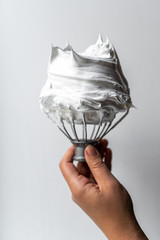 Hand holding whisk with whipped cream