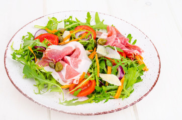 Fresh homemade salad with arugula, jamon, rucola, tomatoes, parmesan.