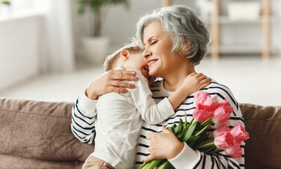 Cheerful little boy giving flowers to grandmother.