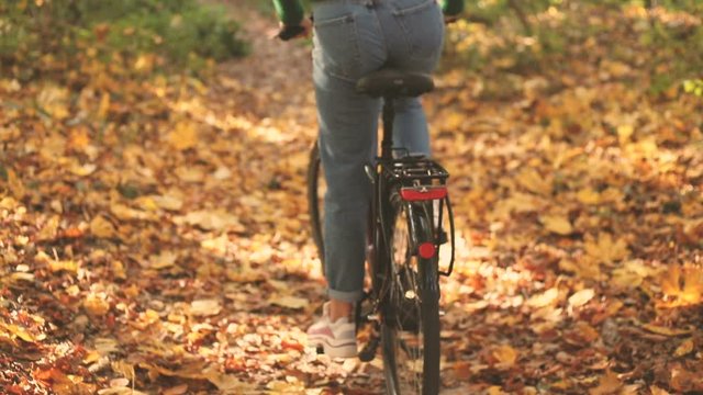 Close up footage of a young girl in jeans and sneakers starting riding her bike, pushing pedals in forest in the autumn morning. Concept of ecological transportation by bike.