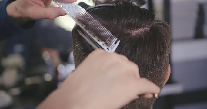 Male barber cutting clients hair with scissors and comb