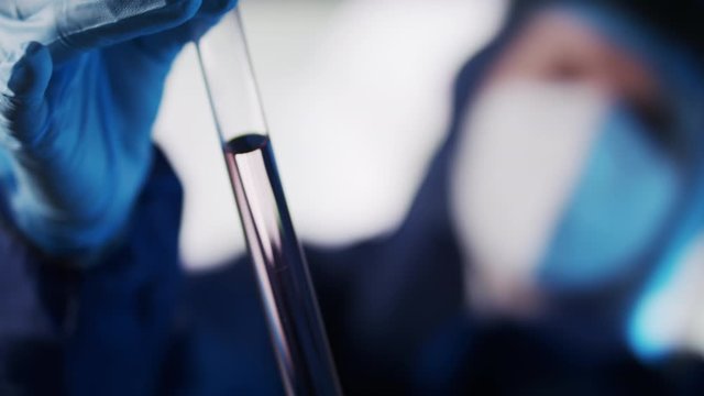 Laboratory analisys and research. Female laborant in protective suit researching sample in glass tube