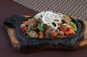 Baked beef with sweet pepper, tomatoes and onions, decorated with onion rings in a cast iron plate in the shape of a cow on a wooden stand