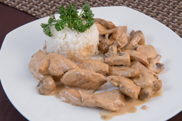 Chicken breast with mushrooms in sour cream on a white plate with a side dish of boiled snow-white rice and a sprig of dill