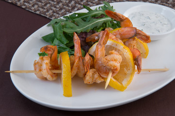King prawns on skewers with lemon slices, a salad of casting greens and milk sauce