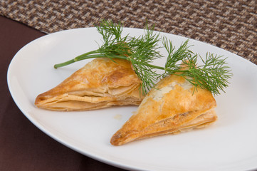 Georgian Khachapuri. Baked puff pastry pie with cheese on a white oval plate with a sprig of dill.