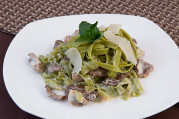 Wide green noodles under sour cream with mushrooms and grated cheese, decorated with slices of cheese and a sprig of mint