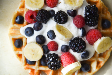Perfect belgian waffle closeup with fresh bananas, strawberries, blackberries, blueberries and whipped cream