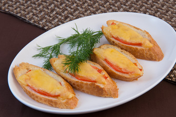 Hot sandwiches. Fried slices of a white baguette with a crispy crust with slices of tomato and cheese, decorated with dill