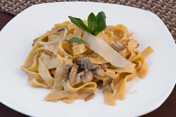 Wide noodles in cheese sauce and with mushrooms, decorated with a sprig of mint and a thin slice of cheese