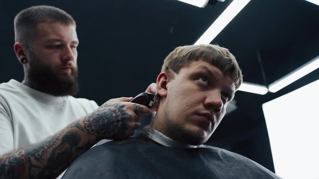 Male haircut with electric razor. Close up of hair trimmer hairstyle. Barber makes haircut for client at the barber shop by using hairclipper. Man hairdressing with electric shaver. Handheld shot. 4K.