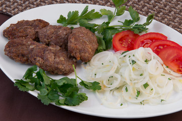 Cutlets fried on a white oval dish with tomatoes, parsley and onion rings