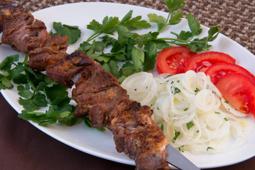 Skewer of lamb meat, parsley, tomatoes, onion cut into rings on a large oval plate