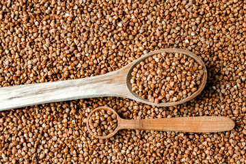 Buckwheat texture. Wooden spoon of roasted buckwheat on buckwheat groat jar background, gluten free ancient grain for healthy diet, selective focus. Coronavirus food supplies. background. top view.