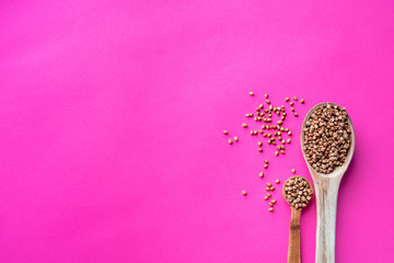 Wooden spoon of roasted buckwheat on buckwheat groat jar background, gluten free ancient grain for healthy diet, selective focus. Coronavirus food supplies. on a pink magenta background. top view.