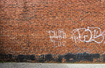 Light white Graffiti and black spray paint on an old yellow brown and red brick wall with grey asphalt road