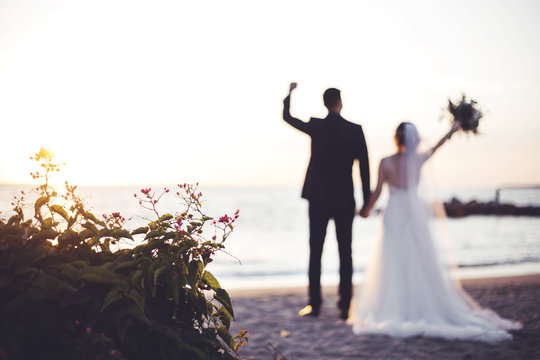 Pareja de novios en la playa levantando las manos con flores en primer plano
