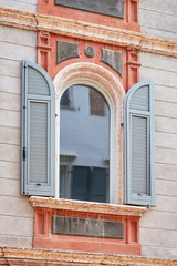 Fototapeta na wymiar Italian window on the stylish and beautiful coloreful wall facade with open wooden grey color classic shutters