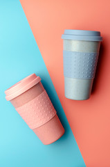 Reusable bamboo coffee cup with silicone holder on colorful background. Flat lay, copy space.
