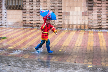 Boy with red raincoat disguised with umbrella splashes in a puddle of water.