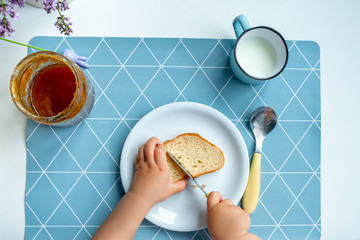 Eating a slice of bread and jam. Little girl eating jam at table in living room. Edible sandwich made of white wheat bread, jam. on a plate in children's hands. Festive Fun Food Concept.