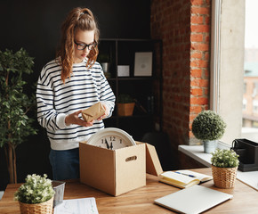 Happy woman newcomer unpacking carton box at table in new workplace in loft office.