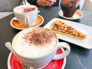 Black stone bistro table with cups of cappuccino and pastries.