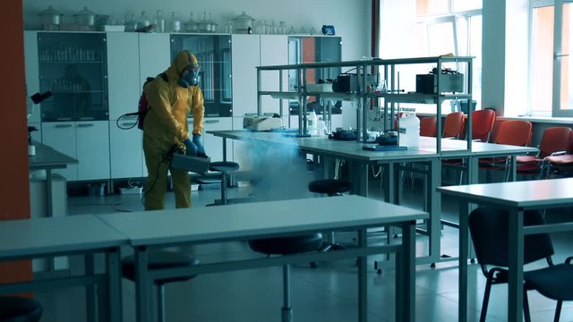 A man in protective suit disinfects a class room.