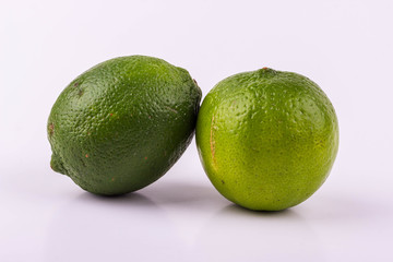 Two delicious, sour green limes lay on a white table against a white background. Limes are great ingredients for cooking.