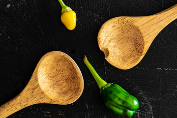 Top view of  two wooden kitchen spoons with bell pepper and jalapeño in a black wooden cooking...