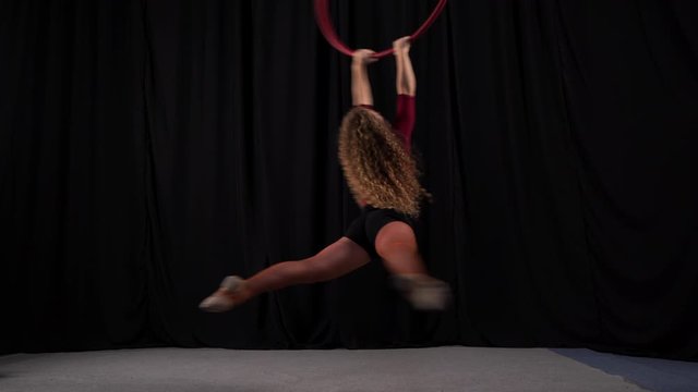 Beautiful curly aerial gymnast. performs elements on aerial hoop against background of black curtain of scene. young flexible European blonde girl spinning fast on circus projectile. aerial ring