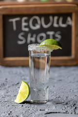 tequila shot garnished with lime slice with chalkboard sign in the back