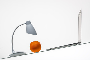 orange under inverted laptop and table lamp on inclined glass table surface isolated on white background   