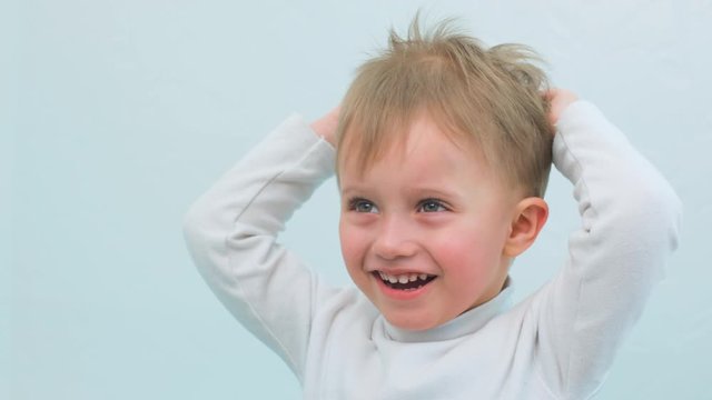 Close up of a little boy in a white sweater, after bathing. The child is having fun, smiling and strokes his hair and doing a hairstyle