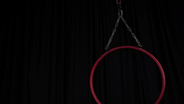 Video of metal red aerial ring for aerial gymnastics with metal chains attached to aerial hoop swinging to sides, circus props, equipment on black background, backstage, coulisse in 4K